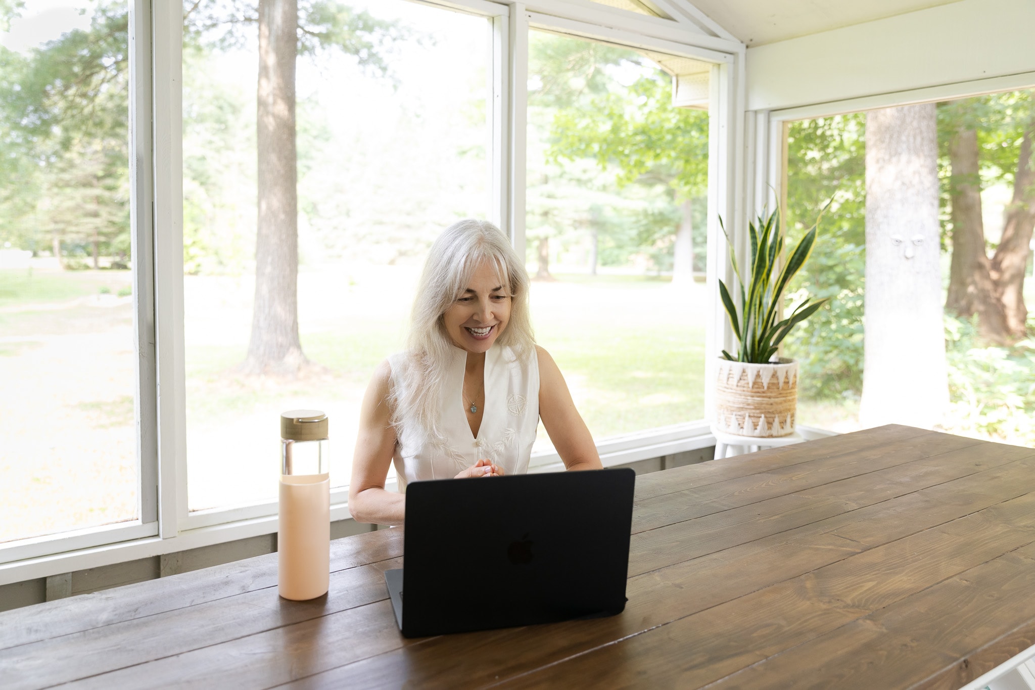 Lori Henein smiling at her laptop on a sunlit screened porch