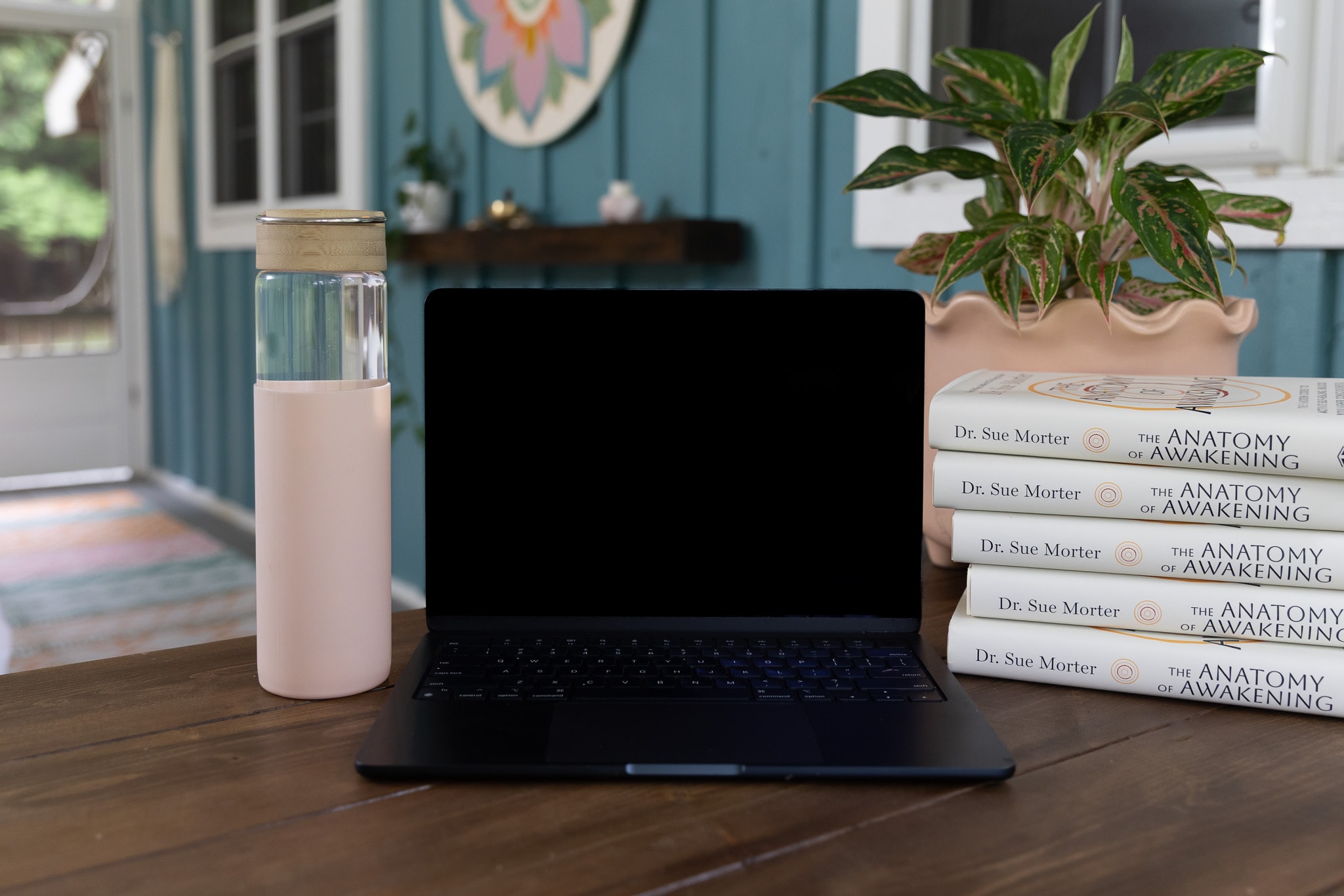Laptop and stacked copies of The Anatomy of Awakening by Dr. Sue Morter on a wooden table